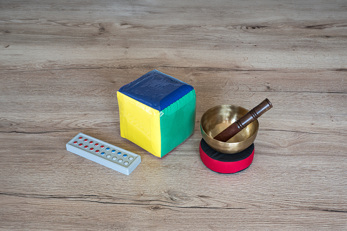 Zähl- und Rechenrahmen aus Kunststoff, Bunter Würfel mit Einstecktaschen und eine Klangschale liegen auf einen Tisch