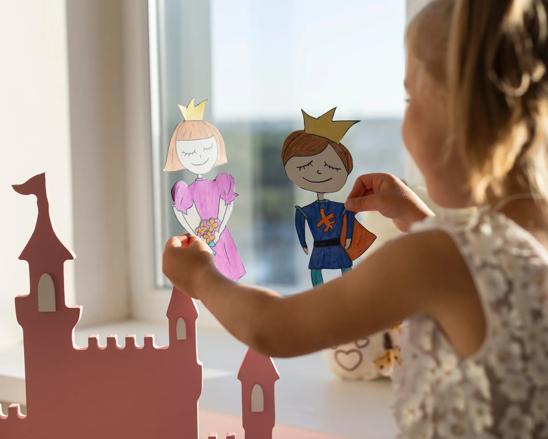 Ein Mädchen spielt mit zwei Pappfiguren Prinz und Prinzessin mit einer Burg im Hintergrund