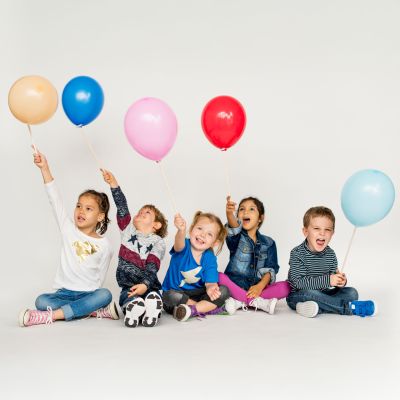 Fünf Kinder sitzen mit verschiedenfarbigen Luftballonen am Boden