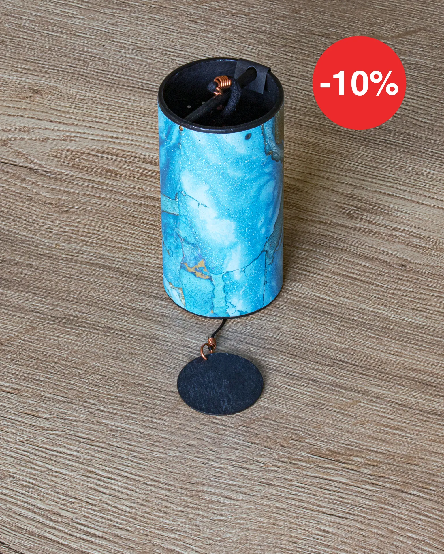 Klangspiel zum Aufhängen liegt auf einen Holztisch, der Klangkörper ist rollenförmig und in blau marmorierter Optik mit goldenen Akzenten