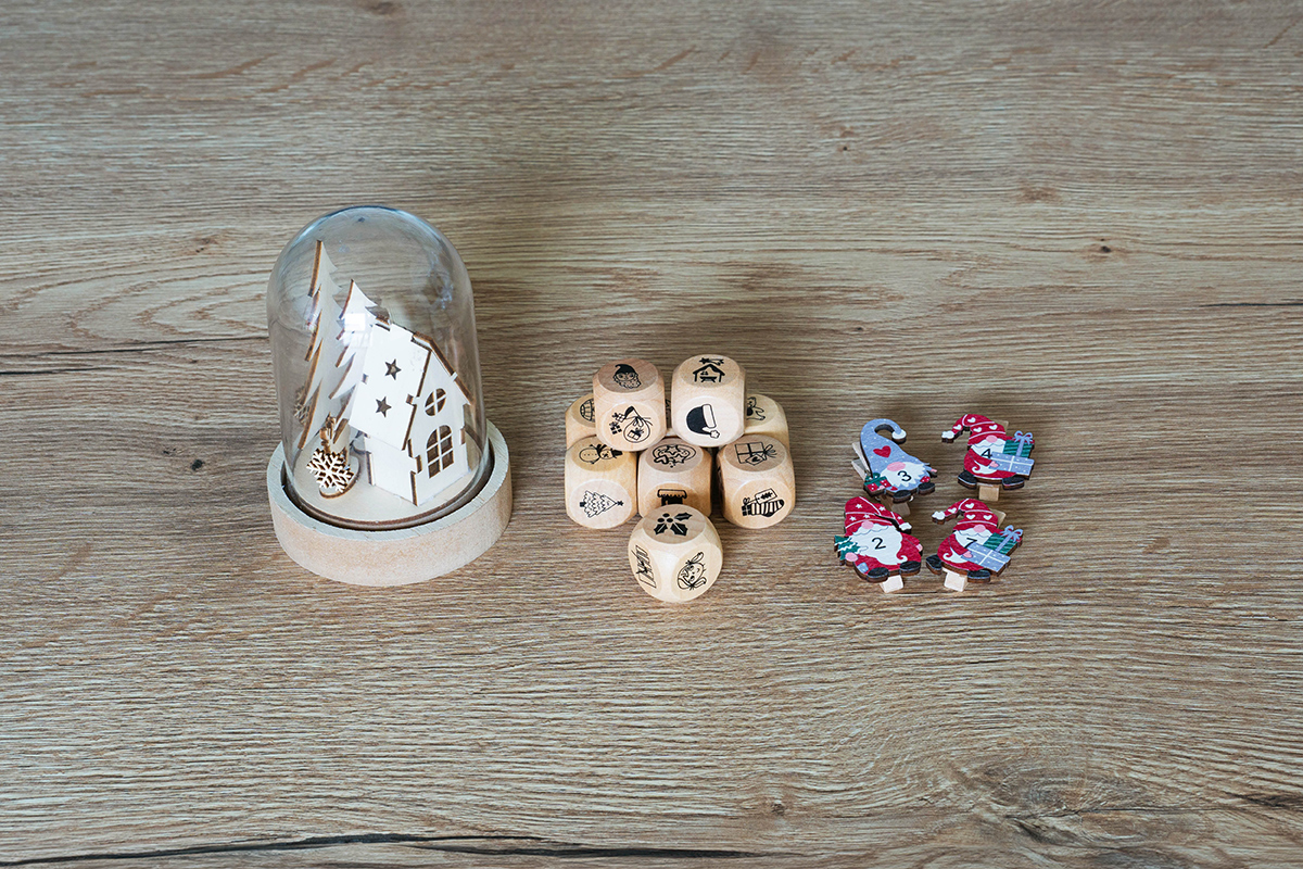 Würfel mit Motiven zu Weihnachten, Adventskalender Klammern und eine Glasglocke mit winterlichen Holzmotiv im Inneren stehen auf einem Tisch