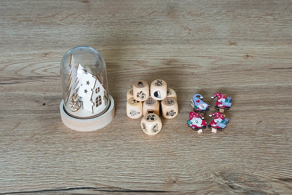 Würfel mit Motiven zu Weihnachten, Adventskalender Klammern und eine Glasglocke mit winterlichen Holzmotiv im Inneren stehen auf einem Tisch