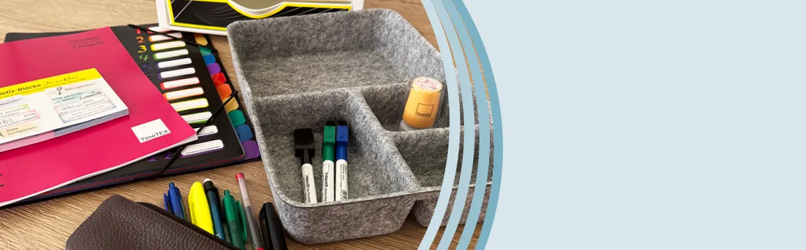 Auf einem Tisch liegen Planer, eine Fächermappe, Haftnotizen und eine graue Organisator-Box aus Filz mit Stiften und Stempeln