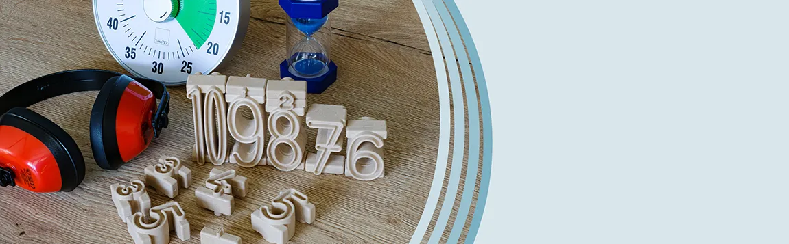Auf einen Tisch liegen ein roter Gehörschutz eine Zeitdauer-Uhr und eine Sanduhr