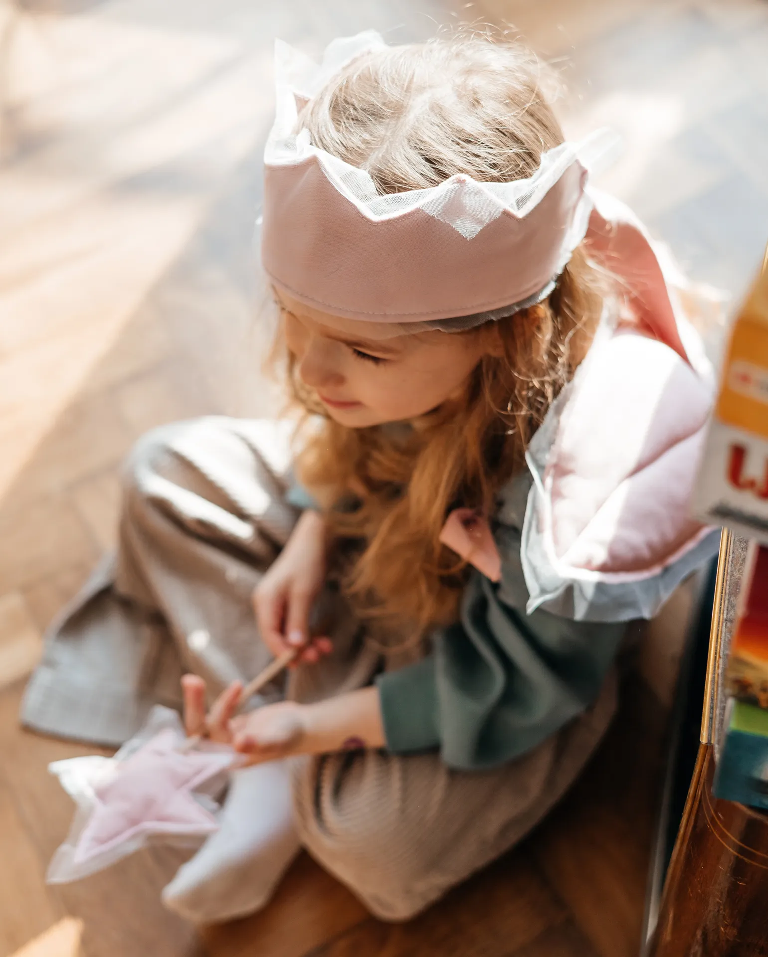 Ein Kind verkleidet als Prinzessin mit einer Krone sitzt auf dem Boden