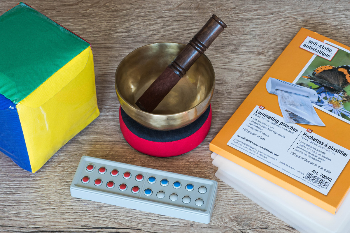 Zähl- und Rechenrahmen aus Kunststoff, Bunter Würfel mit Einstecktaschen und eine Klangschale liegen auf einen Tisch