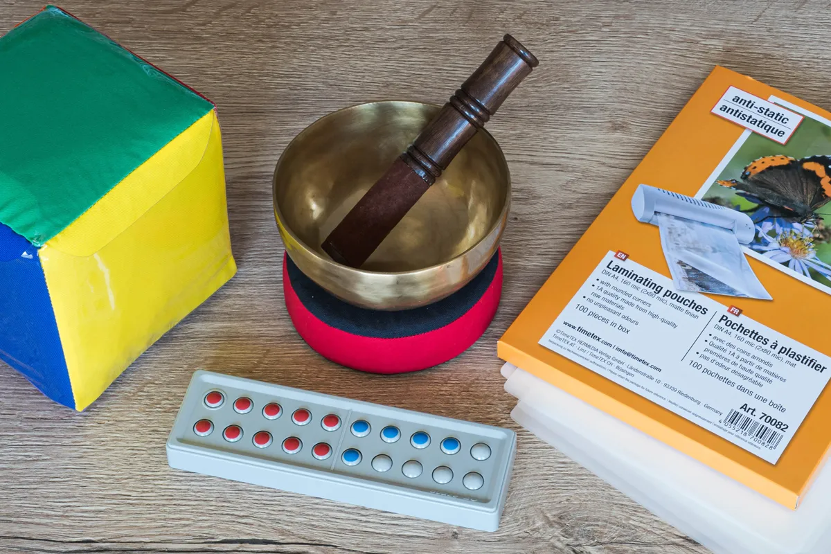 Zähl- und Rechenrahmen aus Kunststoff, Bunter Würfel mit Einstecktaschen und eine Klangschale liegen auf einen Tisch