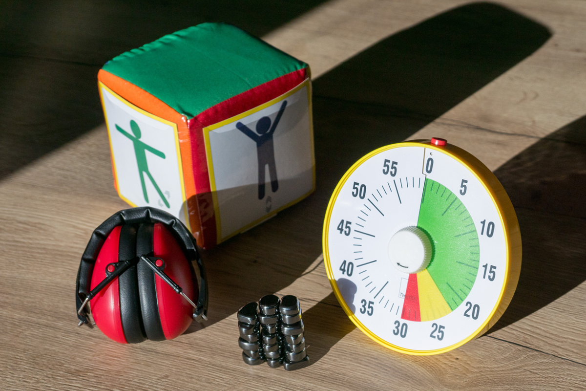 Auf einem Tisch liegen ein Gehörschutz rot, eine Zeitdauer-Uhr und Magnetische Steine