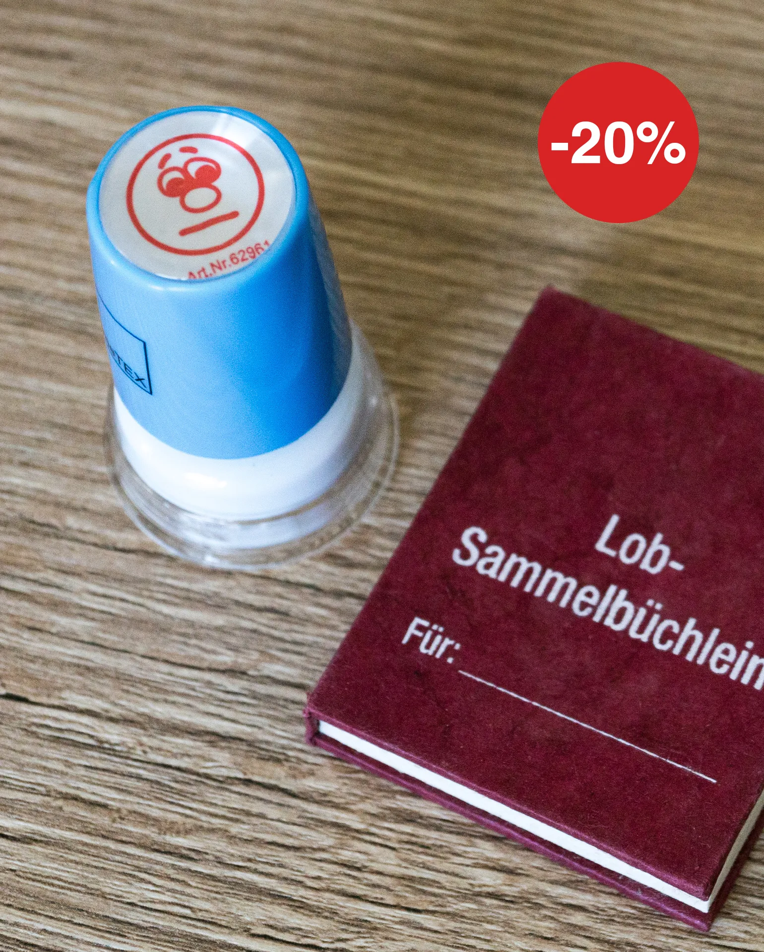 Stempel mit neutralem Gesicht liegt neben einem Lob-Sammelbüchlein auf einem Tisch