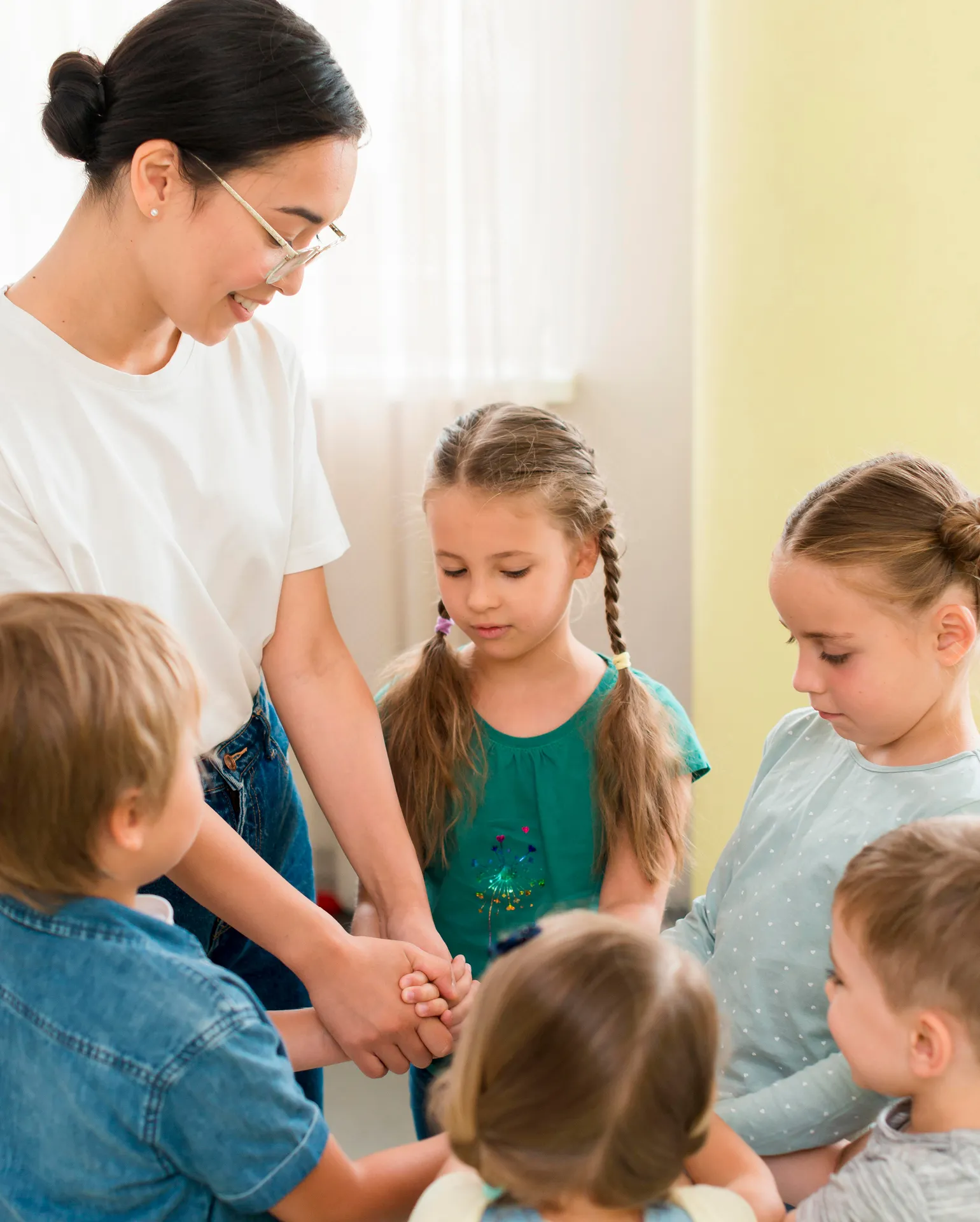 Eine Lehrerin steht im Kreis und hält ihre Kinder an der Hand