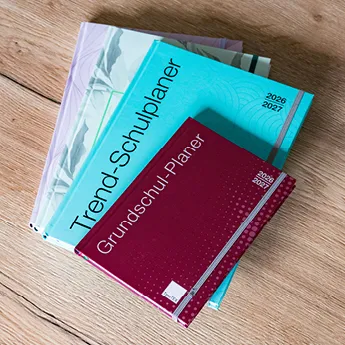 Stapel mit unterschiedlichen TimeTEX Planer wie den Grundschul-Planer und den Trend-Schulplaner liegen auf einem Holztisch leicht gefächert