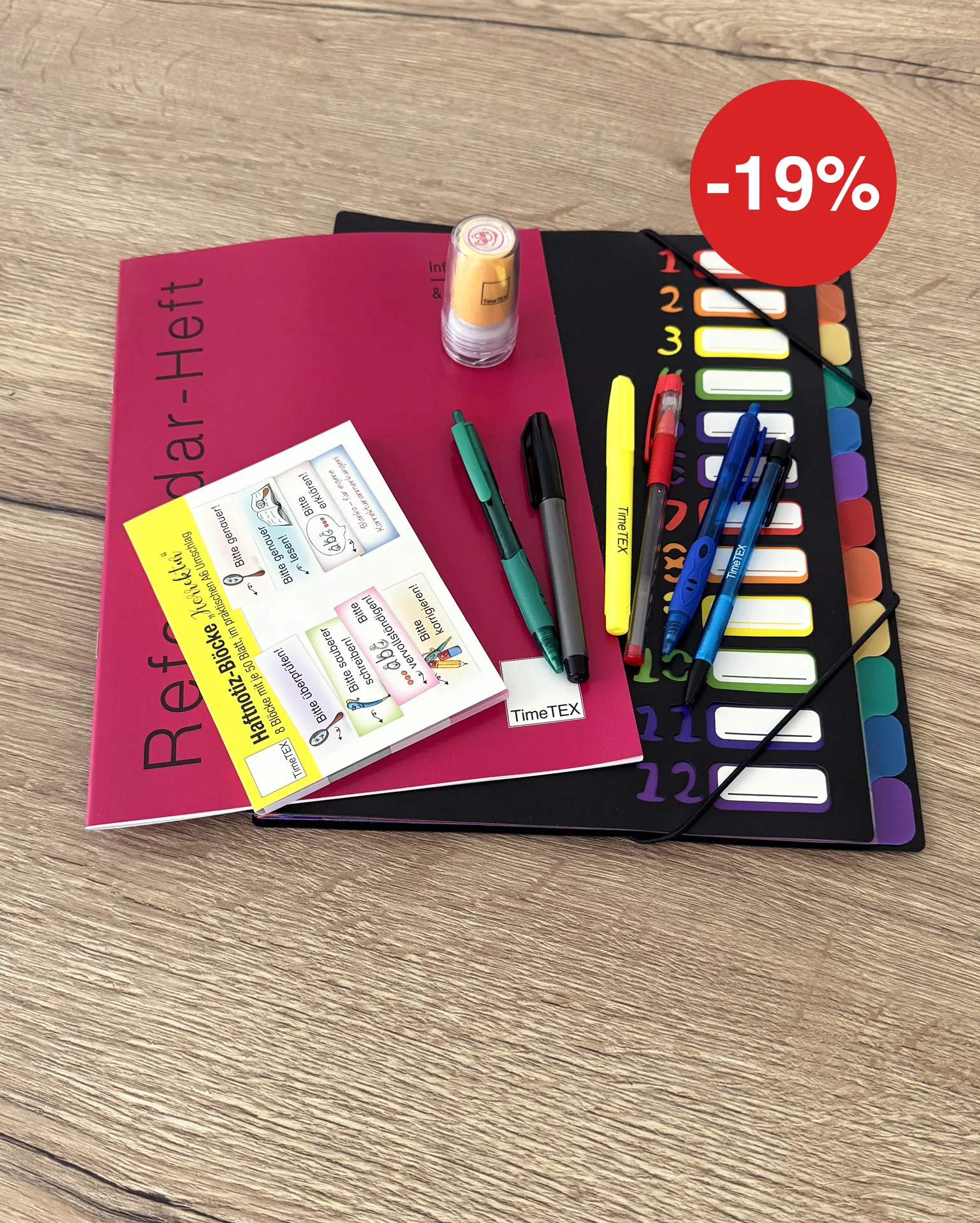 Auf einem Tisch liegen ein rotes Referendar-Heft neben einer Fächermappe, darauf liegen Stifte, ein Stempel und Haftnotiz-Blöcke