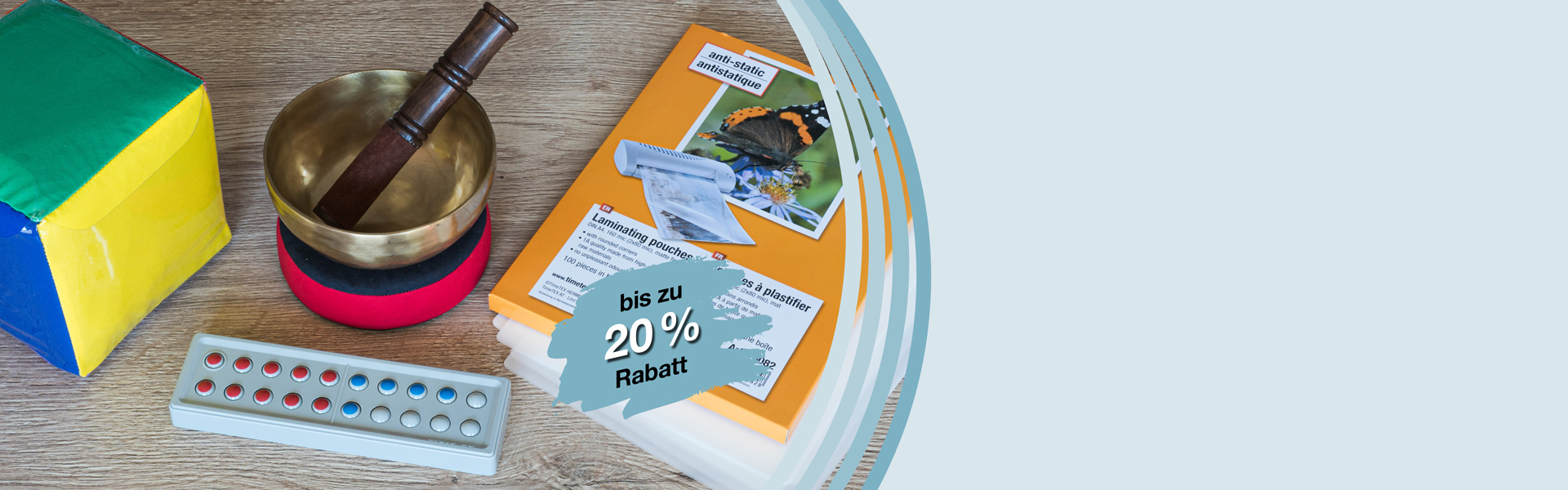 Bunter Würfel mit Einstecktaschen, Klangschale, Laminier-Taschen und ein Zähl- und Rechenrahmen aus Kunststoff liegen auf einen Tisch