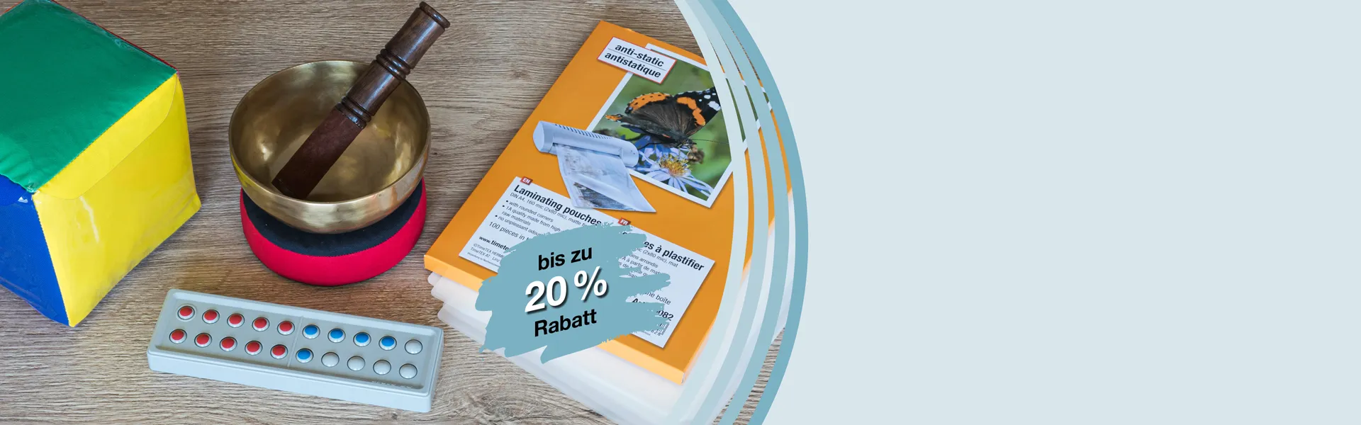 Bunter Würfel mit Einstecktaschen, Klangschale, Laminier-Taschen und ein Zähl- und Rechenrahmen aus Kunststoff liegen auf einen Tisch